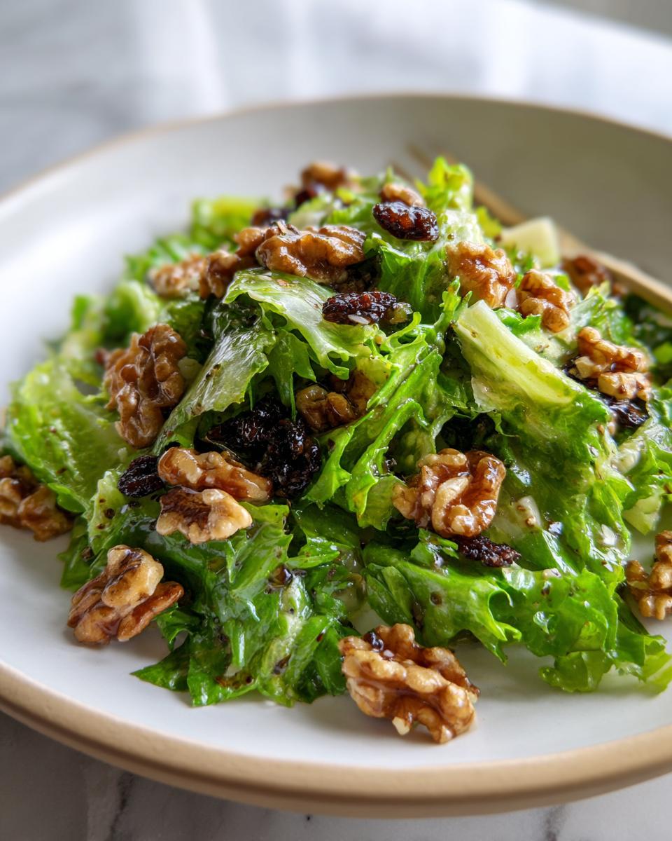 A vibrant portion of celery salad with walnuts and dates mixed with crisp green lettuce, served on a white plate.
