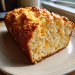 A close-up of a freshly baked slice of cheese beer bread showing a golden crust and melted cheddar bits inside.