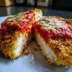 Two halves of crispy chicken parmesan showing the white interior, topped with marinara sauce and melted cheese from the air fryer oven.