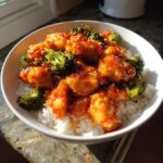 Close-up of a vibrant chicken rice bowl featuring crispy, glazed chicken pieces and bright green broccoli florets over white rice.