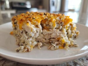 A generous slice of creamy chicken wild rice casserole topped with melted cheddar cheese on a white plate.