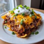 A hearty serving of chili frito pie layered with chili, melted cheese, sour cream, and green onions.