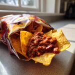 Close-up of a Frito chip topped with hearty chili, taken from an open bag, perfect for a frito pie bar.
