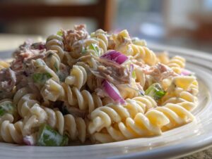 Close-up of creamy cold tuna pasta salad made with fusilli pasta, red onion, and celery.