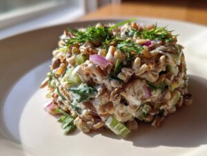 A molded serving of creamy costco grain and celery salad topped with fresh dill.