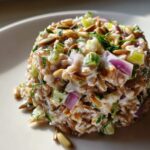 A mound of creamy Costco grain and celery salad mixed with red onion and topped with sunflower seeds.