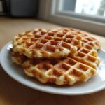 A stack of golden brown cottage cheese waffles healthy piled on a white plate near a bright window.