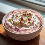 A bowl of pink cranberry jalapeno cream cheese dip, swirled and topped with pecans and chives.