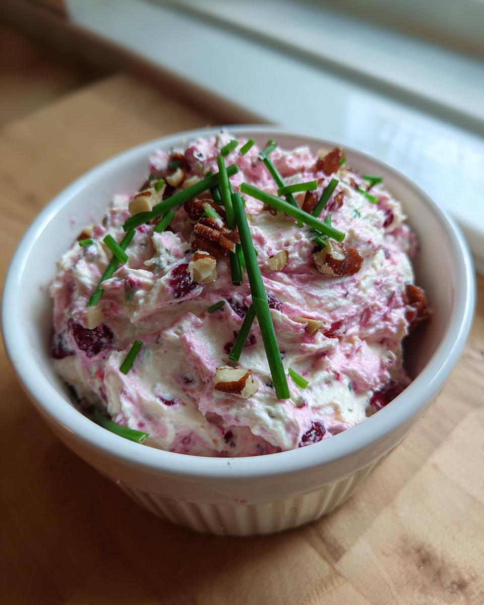 A close-up of cranberry jalapeno cream cheese dip topped with pecans and chives in a white ramekin.