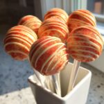 A cluster of bright creamsicle cake pops dipped in white chocolate and orange sprinkles, standing in a white holder.