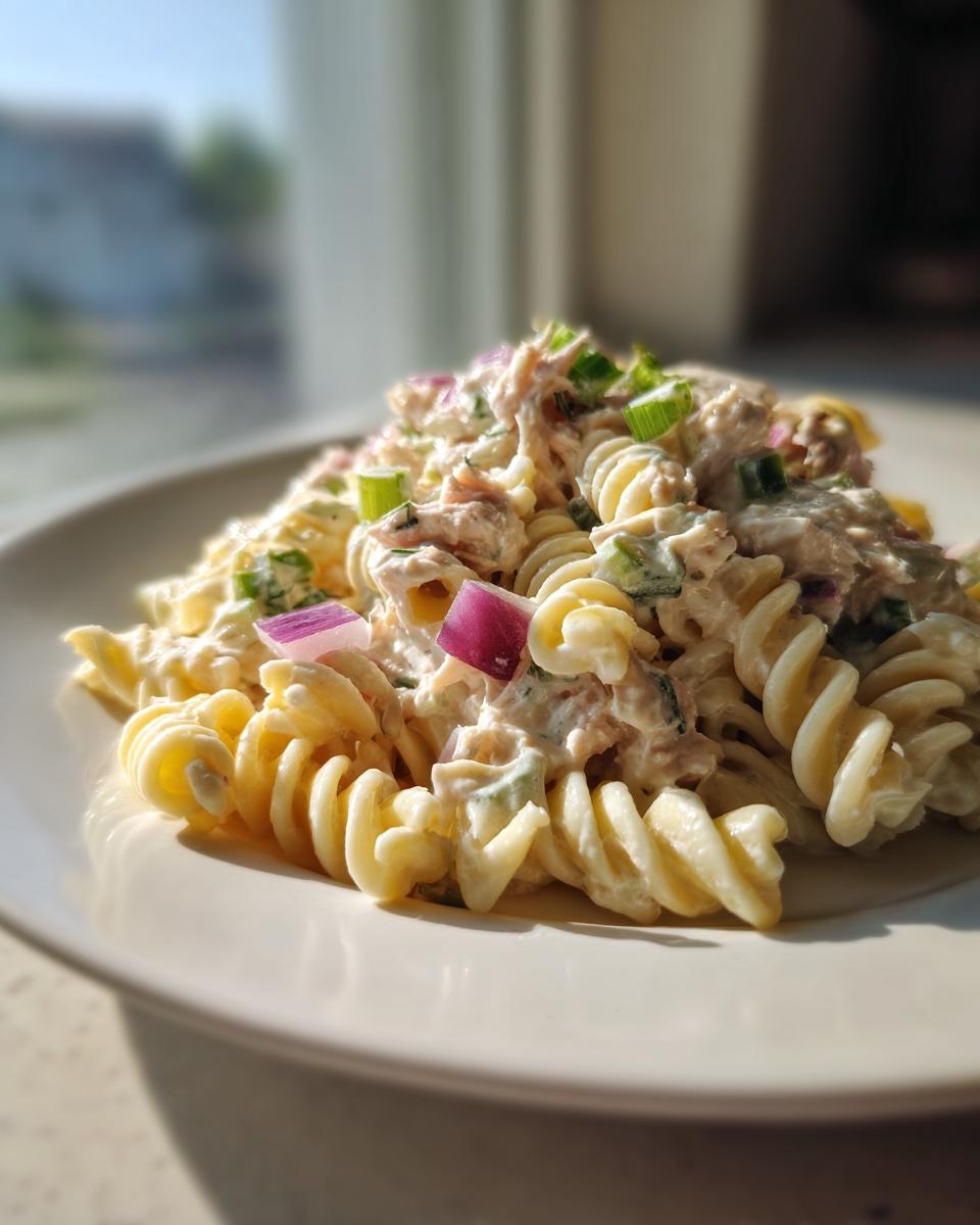 A close-up of creamy cold tuna pasta salad made with rotini pasta, topped with red onion and green onions.