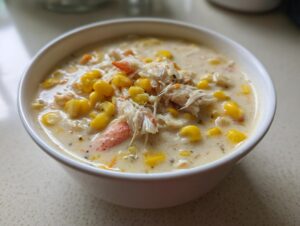 A close-up of a white bowl filled with creamy crab and corn soup, topped with shredded crab meat.