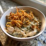 A close-up of a white bowl filled with creamy garlic chicken wild rice casserole, topped with crispy fried onions.