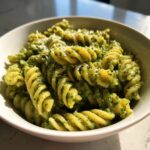 Close-up of creamy pesto pasta made with fusilli noodles, topped with grated cheese.