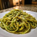 Close-up of fettuccine noodles coated generously in creamy pesto pasta sauce, topped with grated cheese.