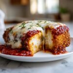 A cross-section view of a crispy chicken parmesan recipe piece, covered in melted mozzarella and marinara sauce.