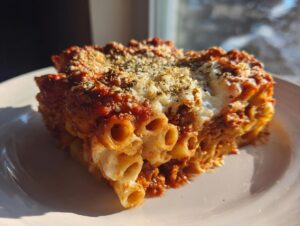 A generous slice of crockpot baked ziti served on a white plate, topped with melted mozzarella and herbs.