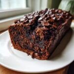 Close-up of a rich, dark slice of double chocolate banana bread topped with melted chocolate chips.