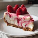 A perfect slice of raspberry cheesecake with a graham cracker crust, topped with fresh raspberries.