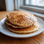 A stack of three fluffy sourdough discard pancakes no eggs drizzled generously with maple syrup on a white plate.