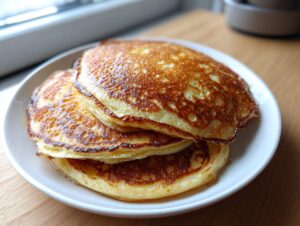 A stack of three fluffy sourdough discard pancakes no eggs, perfectly golden brown on a white plate.