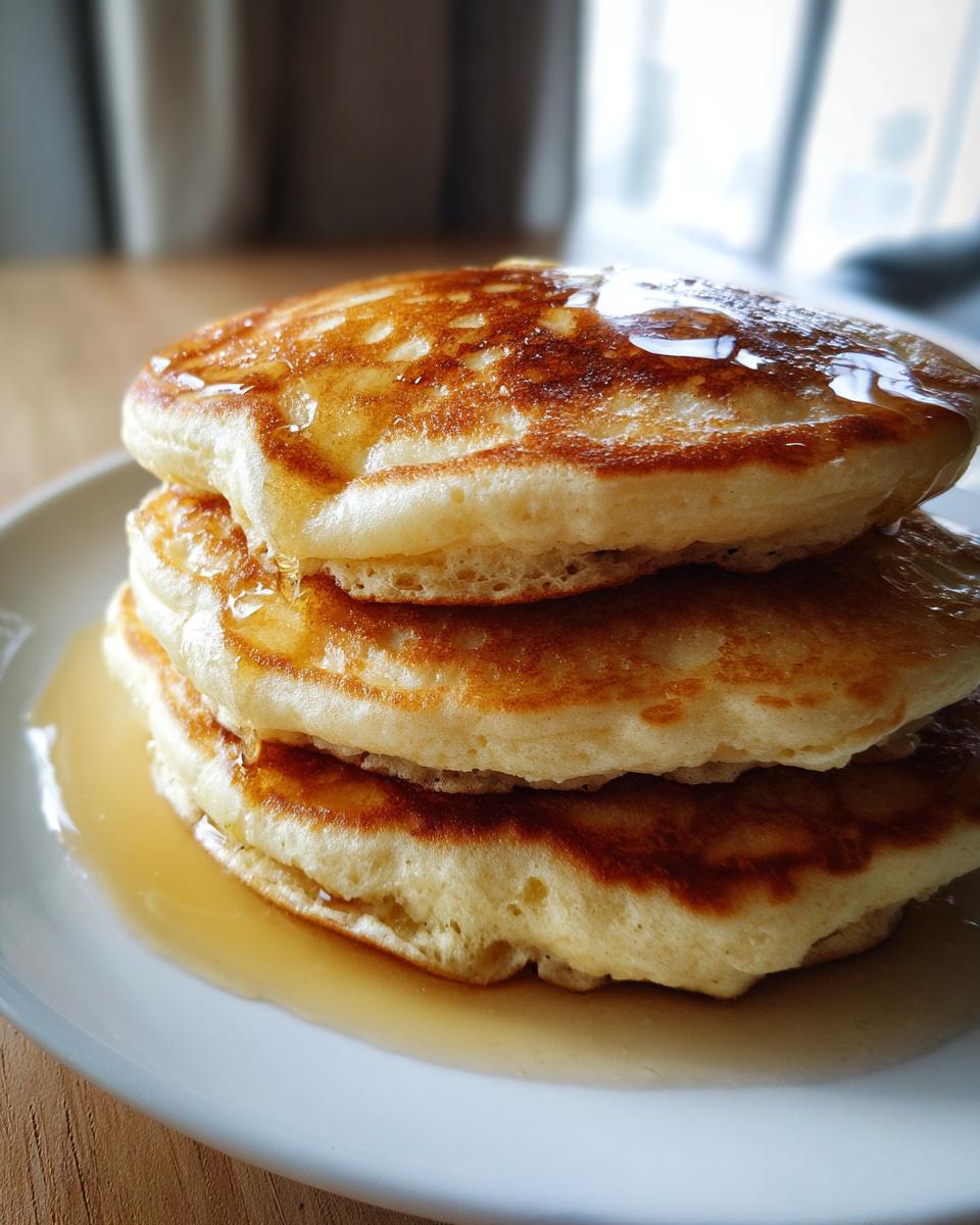 A stack of three fluffy sourdough discard pancakes no eggs drizzled generously with maple syrup.