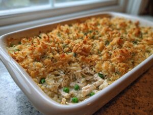 A baked gluten free chicken wild rice casserole in a white dish with a golden, crunchy topping and visible peas.