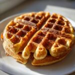 Close-up of a perfectly golden brown, freshly made cottage cheese waffle stacked on a white plate.