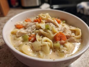 A close-up of creamy instant pot chicken tortellini soup featuring shredded chicken, tortellini, carrots, and celery.