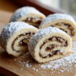 Four slices of italian nut roll cookies, showing the swirled nut filling and generous powdered sugar topping.