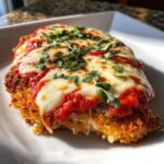 A close-up of a perfectly cooked keto chicken parmesan topped with melted mozzarella, marinara sauce, and fresh basil.