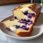 A loaf of lemon blueberry cream cheese bread sliced open to show the swirl of cream cheese and burst blueberries inside.