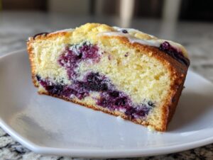 Close-up of a moist slice of lemon blueberry cream cheese bread with visible blueberries and a light glaze.