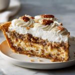 A decadent slice of maple pecan cream pie featuring layers of filling, topped with piped whipped cream and whole pecans.