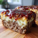 A thick slice of meatloaf casserole with mashed potatoes topping and ketchup glaze.