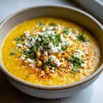 Close-up of a bowl of vibrant yellow mexican street corn soup topped with cotija cheese, chili powder, and cilantro.