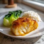Close-up of a perfectly cooked miso glazed chilean sea bass recipe fillet served with white rice and steamed bok choy.
