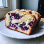 Close-up of a moist slice of Blueberry Cream Cheese Bread showing swirls of cream cheese and burst blueberries.