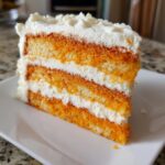Close-up of a moist slice of Creamsicle Cake showing three layers of bright orange cake separated by thick white frosting.