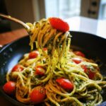 A fork lifting creamy pesto pasta strands topped with a cherry tomato from a black pan, showcasing one pan creamy pesto pasta.
