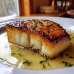 Close-up of a thick, flaky chilean sea bass recipe pan seared fillet with a golden-brown crust sitting in lemon butter sauce.