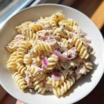 A bowl filled with creamy protein tuna pasta salad featuring fusilli pasta and chunks of red onion.