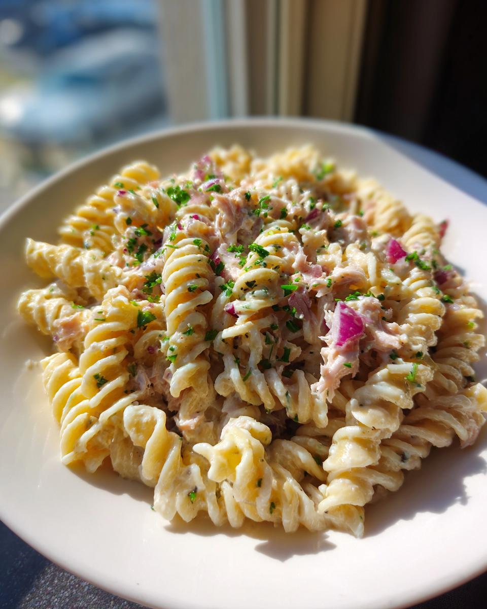Close-up of a bowl of protein tuna pasta salad made with rotini pasta, creamy dressing, red onion, and parsley.