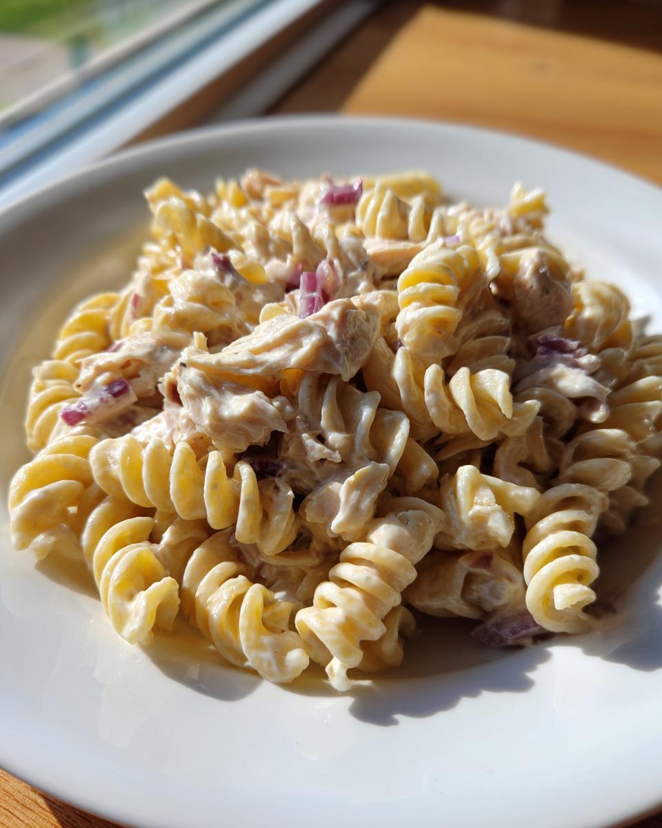 A close-up of a serving of protein tuna pasta salad made with creamy dressing, fusilli pasta, and diced red onion.