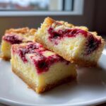 Three delicious raspberry cheesecake bars stacked on a white plate, showing the creamy filling and crumb topping.