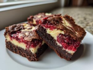 Three rich, fudgy raspberry cheesecake brownies with visible layers of chocolate, cream cheese, and bright red raspberries.