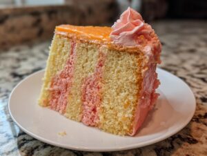 A slice of marbled strawberry creamsicle cake with orange glaze and pink frosting swirl on a white plate.