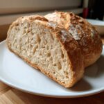 Close-up of a sliced sourdough beer bread showing the open, airy crumb texture on a white plate.
