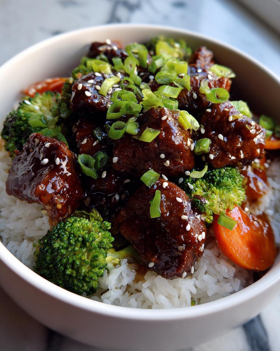 Close-up of a sticky chicken rice bowl featuring glazed chicken pieces, broccoli, carrots, and green onions.