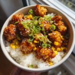 Close-up of a sweet corn chicken rice bowl featuring glazed chicken pieces, corn, and green onions.